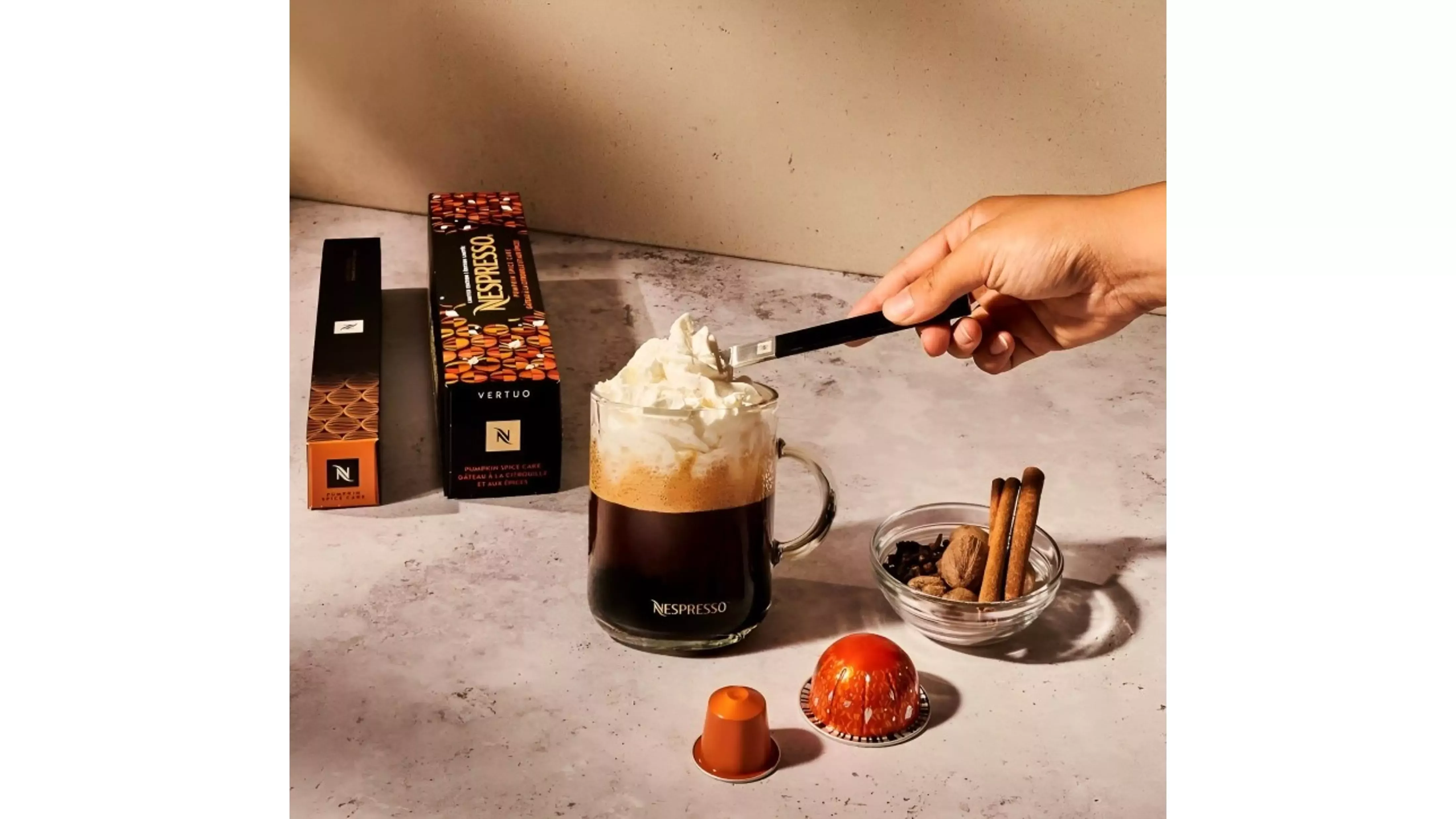 Chávena com café Pumpkin Spice Cake da NESPRESSO em cima de mesa com cápsulas e especiarias